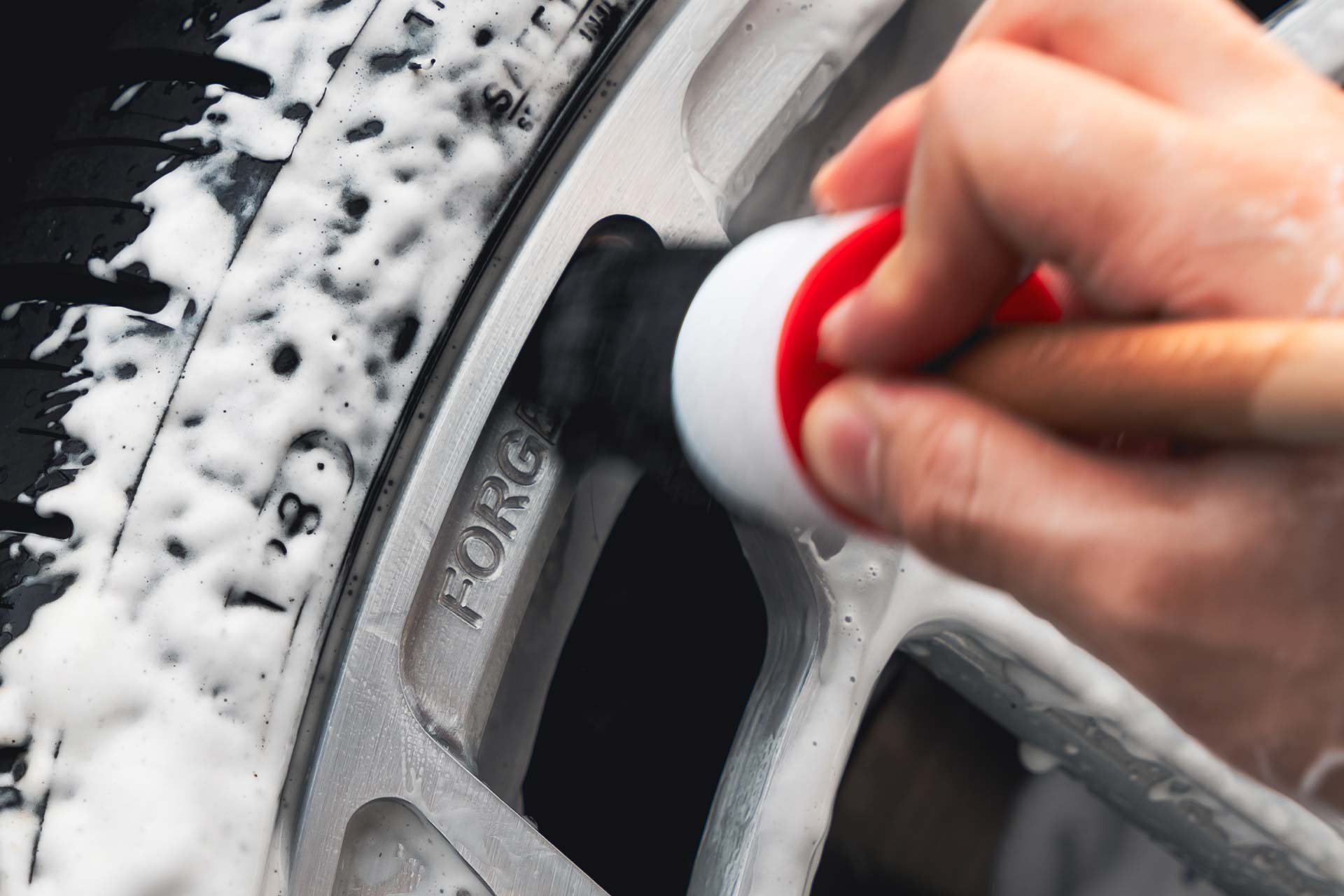 detailer using brush to clean intricate details of forged aluminum wheel